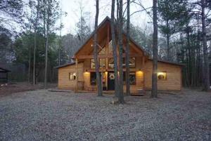 une cabane en rondins dans les bois avec des lumières allumées dans l'établissement The Stunning Shady Creek Cabin, à Broken Bow