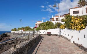 a stone walkway next to a white wall with flowers at Vamos Tenerife - Playa La Arena - Puerto De Santiago in Puerto de Santiago