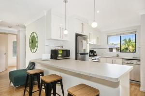 eine weiße Küche mit einer Theke und Stühlen in der Unterkunft Somerset Sunrise Townhouse in Byron Centre in Byron Bay