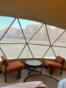 Rum Horizon Camp& Tours في وادي رم: غرفة مع نافذة كبيرة مع كراسي وطاولة