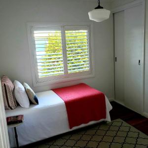 a bedroom with a bed with a red blanket and a window at Boutique Cottage on Mann in Armidale
