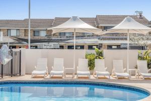 Absolute Beachfront Apartments 3T في لينوكس هيد: مسبح وكراسي ومظلات بجانب سياج