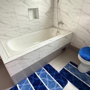a bathroom with a tub and a toilet and a blue rug at Rest Haven Apartments Meanwood in Lusaka +6 photos