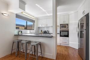 Una cocina con gabinetes blancos y taburetes de bar. en Cosy 2-Bedroom Seaside Unit Steps from Beach, en Maroochydore
