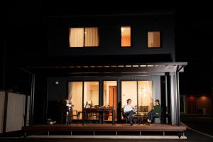 two people sitting on the porch of a house at night at Villas Fuji Terrace ヴィラス富士テラス in Fujikawaguchiko