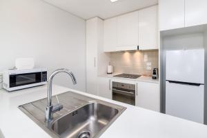 La cuisine blanche est équipée d'un évier et d'un réfrigérateur. dans l'établissement Exquisite Apartment with BBQ and Pool, near Shops, à Phillip