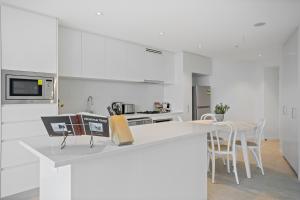 a white kitchen with a counter with a table and chairs at Breathtaking City Views 1-Bed with Pool, BBQ & Gym in Brisbane