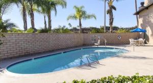 a swimming pool with two chairs and a brick wall at Rodeway Inn Carlsbad in Carlsbad