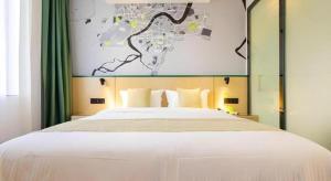 a bedroom with a large white bed with green curtains at Vatica Hotel Haikou Jinniuling Park Haizhiyuan in Haikou