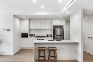une cuisine avec des armoires blanches et un comptoir avec des tabourets dans l'établissement First Floor 3-Bed Stunning Unit by The Ocean, à Kiama
