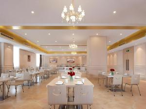 a restaurant with white tables and chairs and a chandelier at Vienna Hotel Anhui Taihe Baitai Xingma International in Taihe