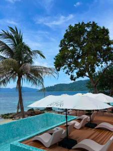 Una piscina con sillas y sombrillas y el océano. en Aya Beach Resort Koh Lipe, en Ko Lipe