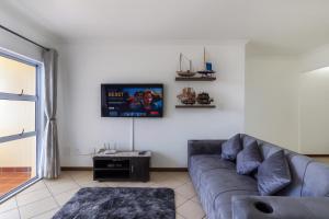 a living room with a couch and a tv on the wall at 606 L'esclaier Cabanas - Seaside Paradise in Amanzimtoti