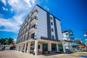 ein hohes weißes Gebäude mit auf einem Parkplatz geparkten Autos in der Unterkunft The Bed Hotel Phitsanulok in Sathani Phitsanulok