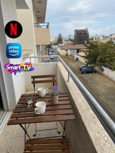 uma mesa de madeira numa varanda com chávenas e flores em Larnaca Comfort Rooms With Smart TV & Netflix em Larnaka