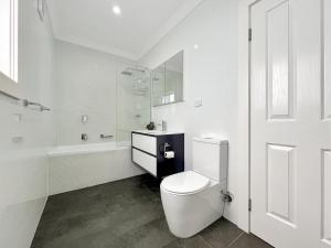 a white bathroom with a toilet and a bath tub at 3-Bed Coastal Haven with Alfresco Dining & BBQ in Marks Point