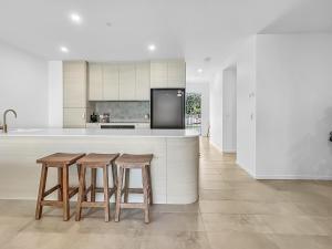 cocina con 2 taburetes y encimera con nevera en 3-Bed: Riverfront Alfresco Dining & Rooftop Pool, en Batemans Bay
