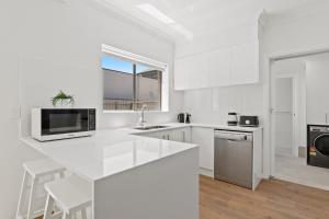 une cuisine blanche avec un évier et un micro-ondes dans l'établissement Elegant 3-Bed Home Steps from Sunny Glenelg Beach, à Glenelg 18 autres photos