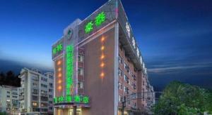 Un bâtiment avec des lumières vertes sur son côté dans l'établissement GreenTree Inn Yantai Xingfu Road Marina Plaza Express Hotel, à Yantai