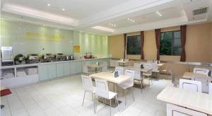 a restaurant with tables and white chairs and a kitchen at City Comfort Inn Jiangmen Xinhui Xiangshan Park in Xinhui