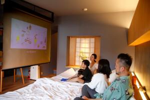 a group of people sitting on a bed watching a screen at Temari Inn Madoromi in Kurashiki