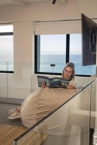 a woman laying on a bed reading a book at Oceanfront Duplex Apartments, Hermanus Waterfront in Hermanus