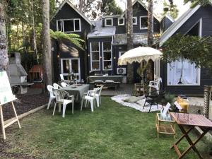 Un patio trasero con sillas y mesas blancas y una casa. en Relax in Titirangi Cozy Studio Apartment, en Parau