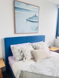 een bed met een blauw hoofdeinde met een schilderij aan de muur bij Azure View One-Bed in Gold Coast