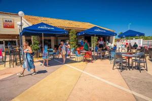 Eine Gruppe von Menschen spaziert auf einer Terrasse mit blauen Sonnenschirmen. in der Unterkunft Camping 4 étoiles - Parc aquatique - ccadfdf in Saint-Jean-de-Monts