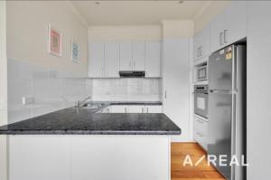 una cucina con mobili bianchi e un frigorifero in acciaio inossidabile di Central Melbourne 2BR Balcony Apartment a Melbourne