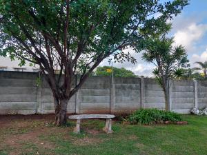 a bench sitting under a tree next to a fence at Coda in Umkomaas