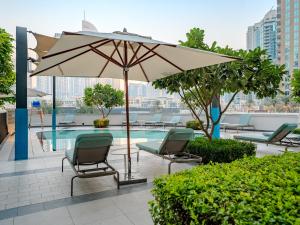 eine Terrasse mit Stühlen und Sonnenschirm und ein Pool in der Unterkunft Ahlan HH - Burj Khalifa and Fountain Views Suite at Grande Downtown in Dubai