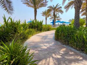 ein Weg mit Palmen und ein Strand mit Sonnenschirmen in der Unterkunft Island Bliss 2 BR with Private Beach and Pool in Al Marjan Island in Ras al Khaimah