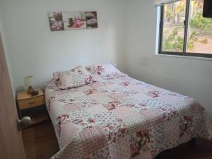 a bedroom with a bed with a quilt and a window at Cabañas Tinaja y Sauna Laguna Verde Valparaiso in Valparaíso