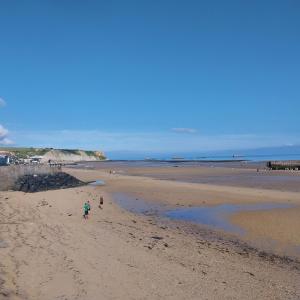 two people are walking on a sandy beach at Studio De La Mer in Arromanches-les-Bains