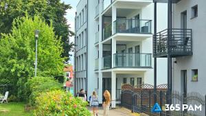 two people walking down a sidewalk in front of a building at 365PAM - Apartament Leaf 6-osobowy in Ustronie Morskie