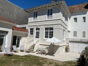 a white house with chairs and an umbrella at Villa 6 personnes proche marché du Touquet avec jardin - FR-1-821-26 in Le Touquet-Paris-Plage