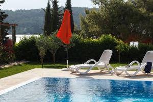a swimming pool with two lawn chairs and an orange umbrella at Villa Marin in Sutomišćica