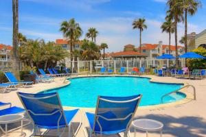 a swimming pool with blue chairs and palm trees at Beach Club 323 in Padre Island