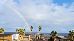 a rainbow over a beach with palm trees and a building at Terraza al mar in Candelaria +11 photos