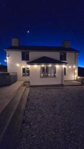 una casa blanca con luces al costado de ella por la noche en Cwm Uchaf Holiday Home, hot tub and horse view!, en Abergele