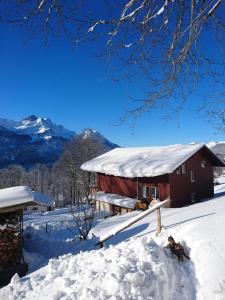 un granero rojo cubierto de nieve con montañas al fondo en Obererli, en Hasliberg
