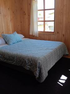 a bed in a wooden room with a window at VERDEAGUA Hostal in Chaitén