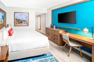 Compass Hotel Beaufort by Margaritaville في Beaufort: غرفة فندقية تحتوي على سرير ومكتب وتلفزيون