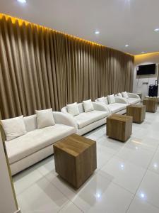 a living room with white couches and wooden tables at واحه فدك للشقق المخدومه in Al Ḩāyiţ