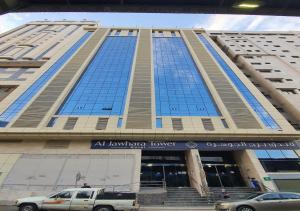 a large building with blue windows and a truck parked in front at Al JAWHRA TOWER HOTEL in Mecca