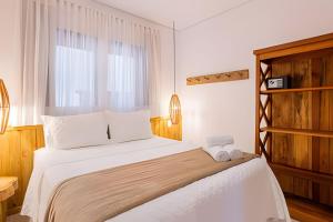 a bedroom with a bed with white sheets and a window at Apê Rustic Chic na Rua do Mucugê - Café da manhã opcional - Estilo e Localização Premium in Porto Seguro +65 photos