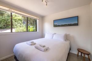 a bedroom with a large white bed and a window at Birdsong Sanctuary - Be My Guest Waiheke in Waiheke Island