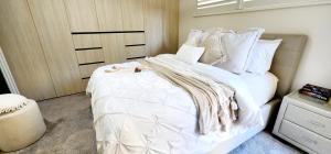 una habitación con una cama grande con sábanas y almohadas blancas en Cerulean Apartments, en Caloundra