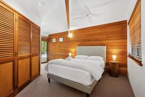Noosa Retreat. Ocean Views, Pool and Serenity في نوسا هيدز: غرفة نوم بسرير ابيض وجدران خشبية +8 صور